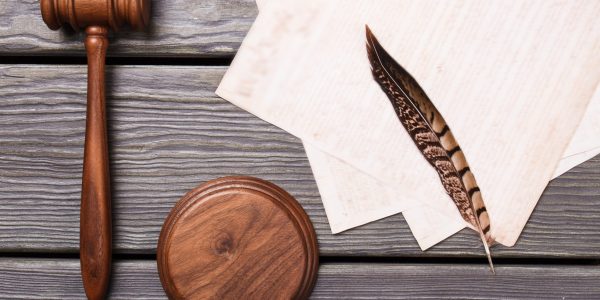 Flat lay wooden gavel and feather. Top view trial accessories with papers.